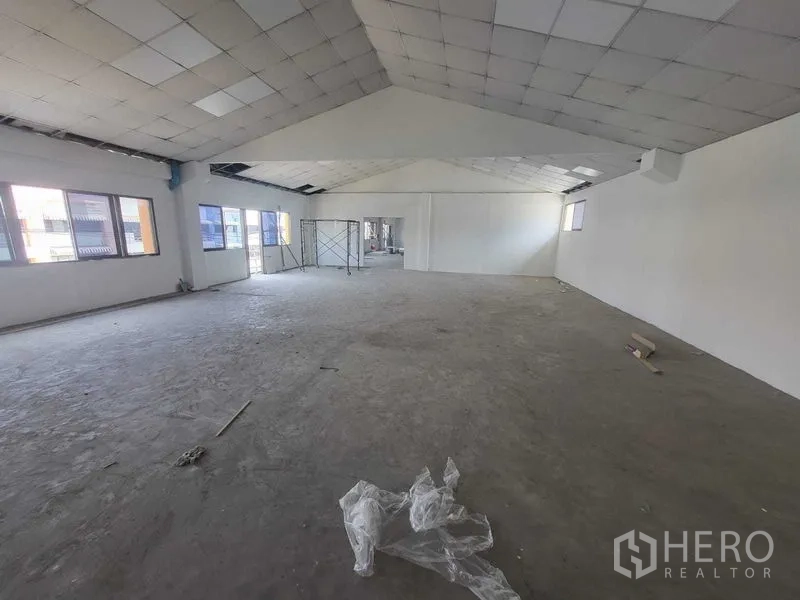 Factory for rent or sale in Samut Prakan - Large top-floor workspace with pitched ceiling tiles, windows and scaffold frame.