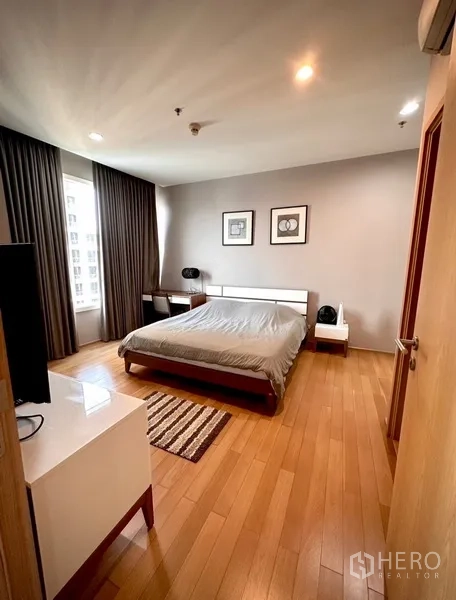Condominium for rent or sale in Watthana, Bangkok - Spacious bedroom with double bed, bedside tables, large window and drapes on wooden flooring.