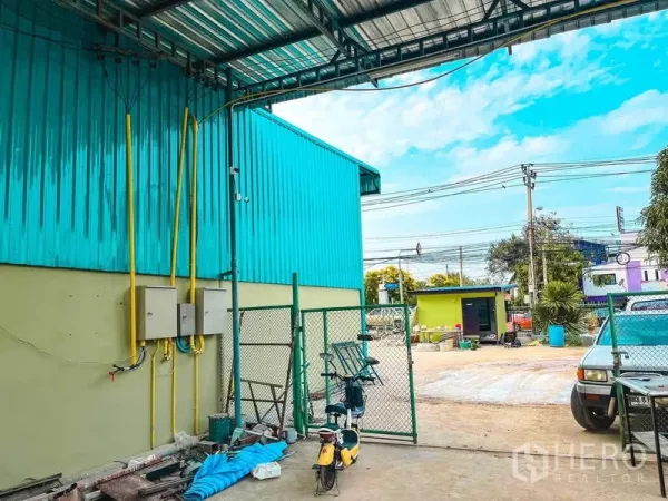 Warehouse for rent in Sai Mai, Bangkok - Side yard featuring a covered loading bay, utility boxes and a fenced access gate beside the warehouse.