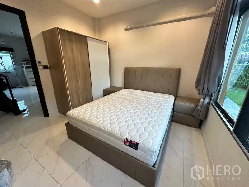 Detached House for rent in Bang Phli, Samut Prakan - Ground-floor bedroom with an upholstered bed, bedside table, wardrobe and garden-view window.