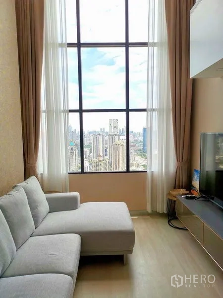 คอนโด ให้เช่าในSathon, Bangkok - ห้องนั่งเล่นมีหน้าต่างสูงจรดเพดาน โซฟาเข้ามุมสีเทา ตู้วางทีวี และวิวสกายไลน์กรุงเทพฯ