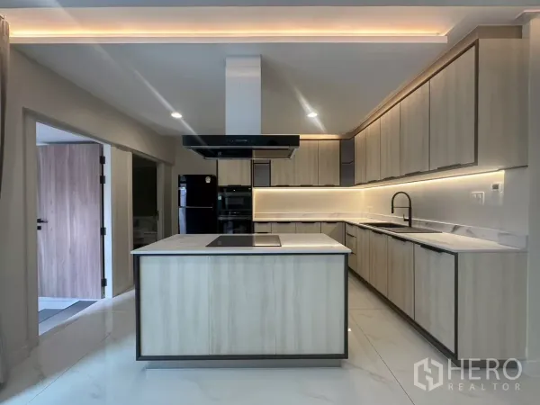 Townhouse for rent in Watthana, Bangkok - Contemporary island kitchen with light wood cabinetry and under-cabinet lighting.