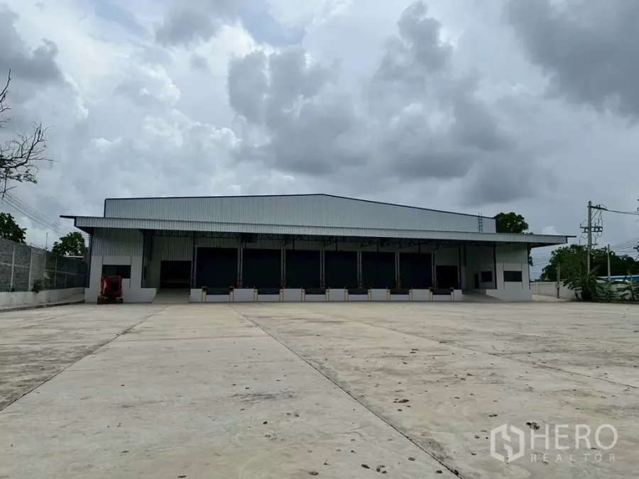 Warehouse for rent in Si Racha, Chon Buri - Front of stand-alone warehouse in Si Racha with wide concrete yard and covered loading docks.