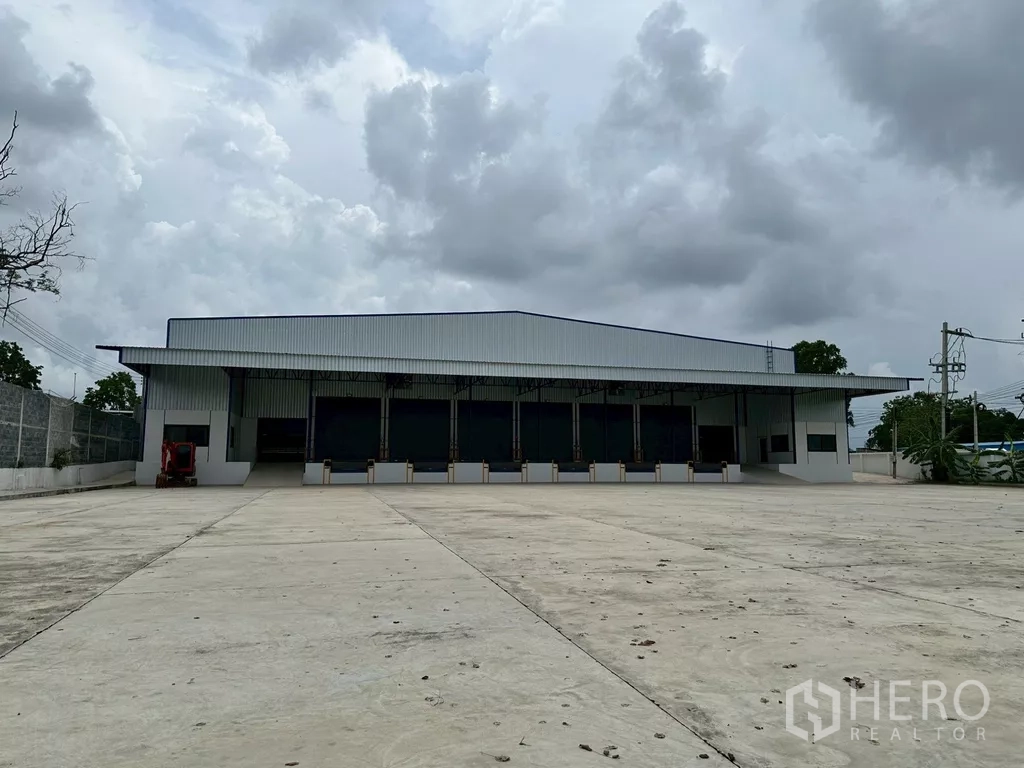 Warehouse for rent in Si Racha, Chon Buri - Front of stand-alone warehouse in Si Racha with wide concrete yard and covered loading docks.