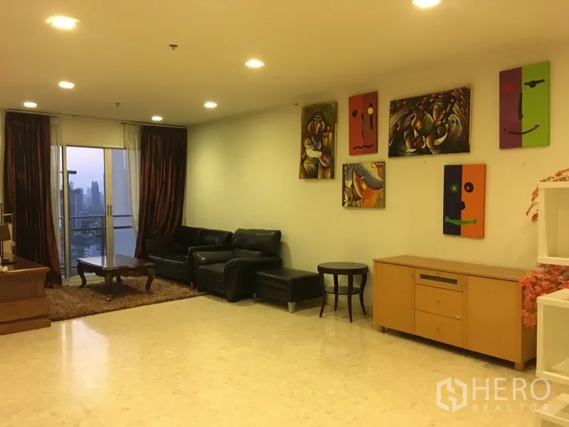 Condominium for rent in Khlong Toei, Bangkok - Spacious living room with black leather sofa, recessed lighting, balcony doors, and skyline view.