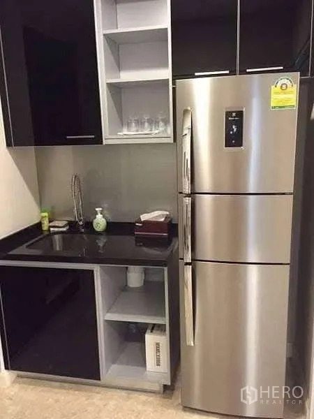 Condominium for rent in Khlong Toei, Bangkok - Kitchen corner with sink, black cabinetry and stainless-steel refrigerator.