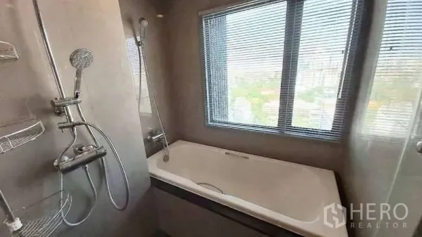 Condominium for rent in Khlong Toei, Bangkok - Bathroom with bathtub and shower beside a large window offering a city view.