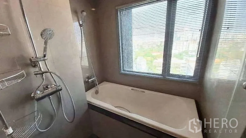 Condominium for rent in Khlong Toei, Bangkok - Bathroom with bathtub and shower beside a large window offering a city view.