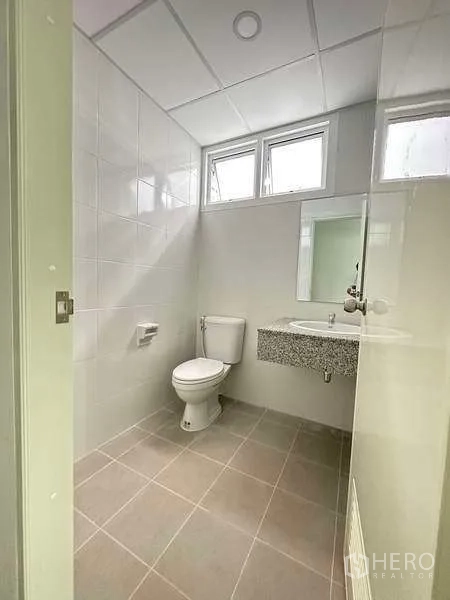 Factory for rent in Khlong Luang, Pathum Thani - Clean tiled restroom with toilet, sink and daylight windows.