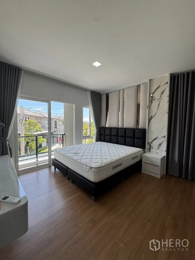 Detached House for rent in Bang Phli, Samut Prakan - Master bedroom with king bed, floor-to-ceiling windows, balcony access and wood flooring.