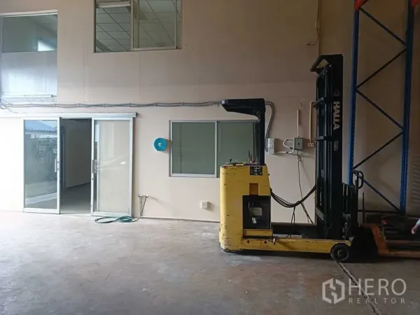 Warehouse for rent in Suan Luang, Bangkok - Indoor loading area with a yellow forklift beside office windows and a sliding glass door.
