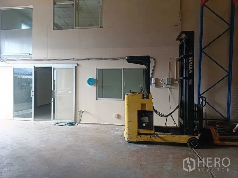 Warehouse for rent in Suan Luang, Bangkok - Indoor loading area with a yellow forklift beside office windows and a sliding glass door.