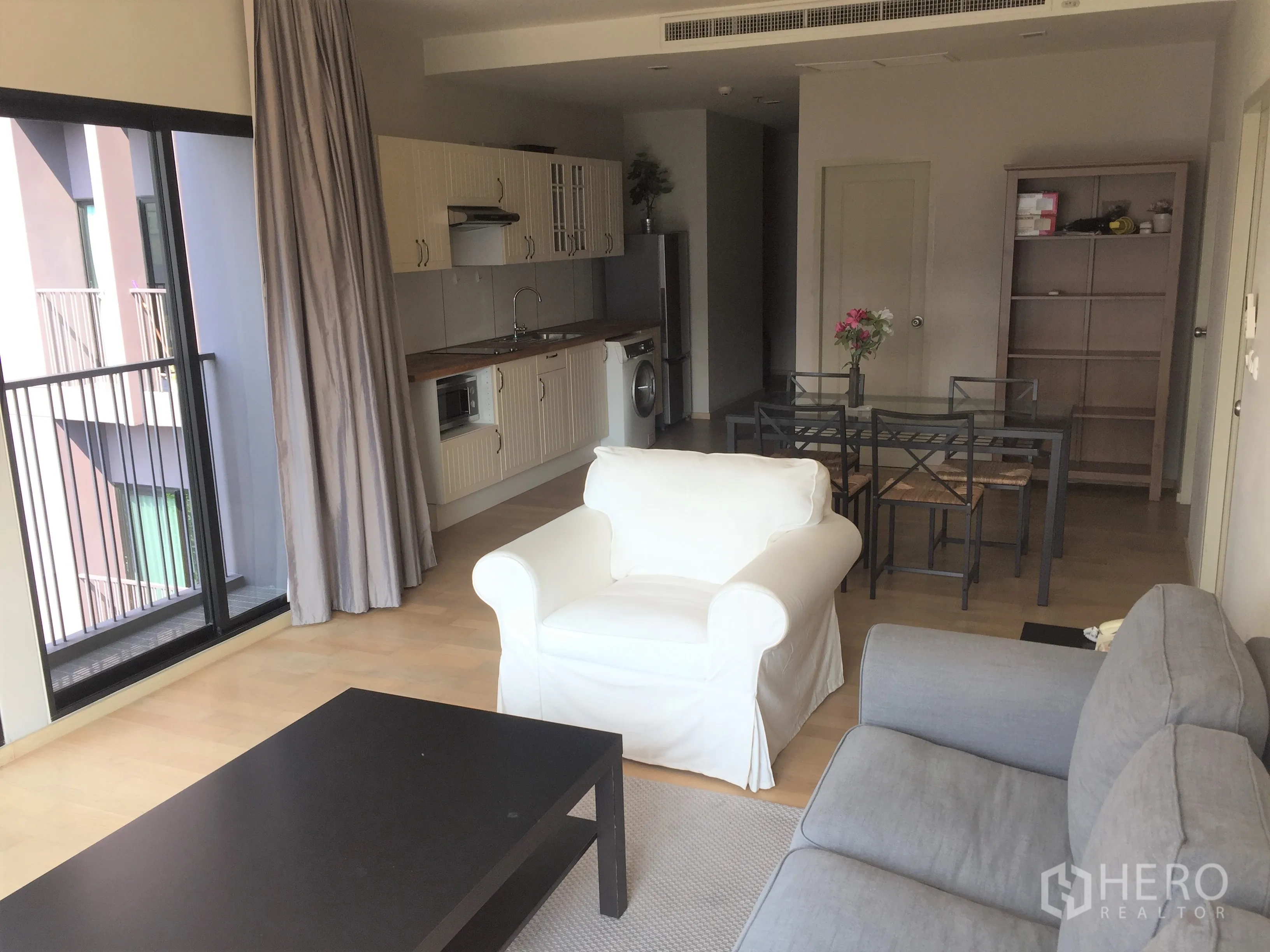 คอนโด ให้เช่าหรือขายในWatthana, Bangkok - ห้องนั่งเล่นแบบโอเพนโปร่งสว่าง มีประตูบานเลื่อนไปยังระเบียง พื้นไม้ โซฟา และครัวบิลท์อิน