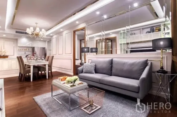 Condominium for rent in Huai Khwang, Bangkok - Stylish living room with gray sofa, mirrored feature wall, black lamps and open dining area on wood floors.