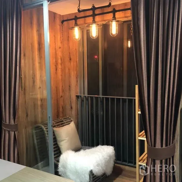 Condominium for rent or sale in Phra Khanong, Bangkok - Cozy balcony nook with industrial pendant lights, wood paneling and a cushioned lounge chair.