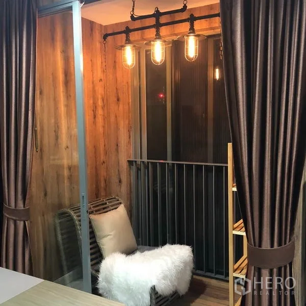 Condominium for rent or sale in Phra Khanong, Bangkok - Cozy balcony nook with industrial pendant lights, wood paneling and a cushioned lounge chair.