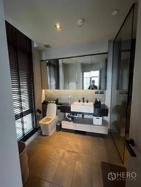 Condominium for rent in Watthana, Bangkok - Bathroom with large mirror, vanity, toilet and window blinds.