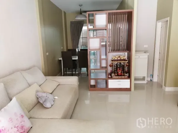 联排别墅 出租在Wang Thonglang, Bangkok - 明亮客厅，L 型沙发与亮面瓷砖地面，装饰隔断通向餐区。