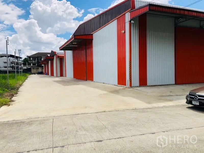 Warehouse for rent in Wang Thonglang, Bangkok - Row of red steel warehouses with a spacious driveway suitable for trucks and parking.