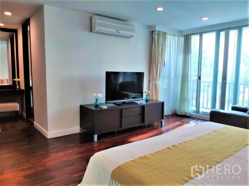 Condominium for rent in Bang Rak, Bangkok - Master bedroom view with TV console, air conditioning and balcony access via sliding doors.