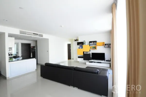 Condominium for sale in Khlong San, Bangkok - Bright open-plan living room with black sectional sofa, TV wall and open kitchen in a Bangkok condo.