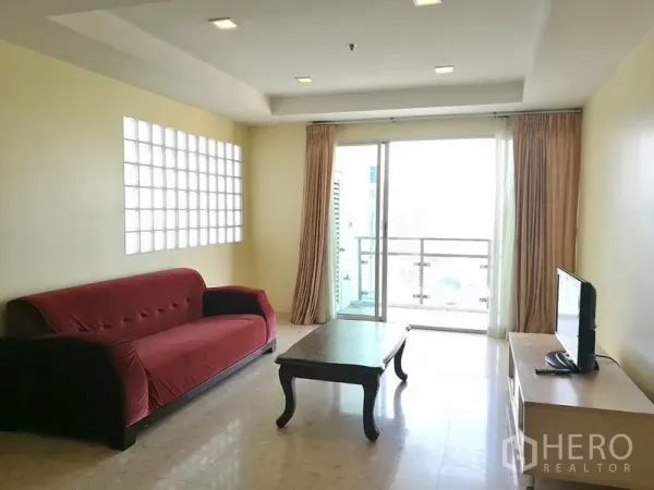 Condominium for rent in Khlong Toei, Bangkok - Bright Ekkamai-area condo living room with red sofa, TV console, and balcony doors.