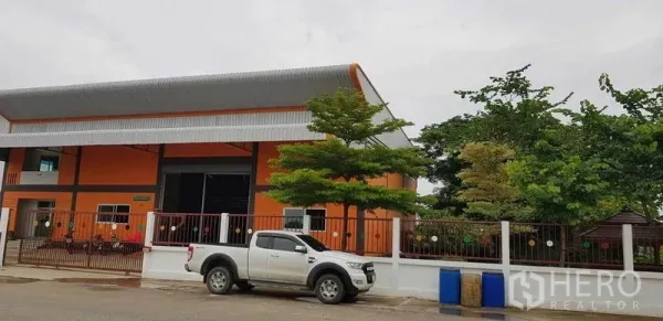 工厂 出售在Bang Phli, Samut Prakan - 街景视角的橙色仓厂建筑，设围栏大门与皮卡车。