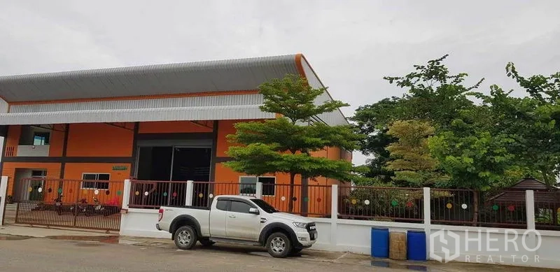 工厂 出售在Bang Phli, Samut Prakan - 街景视角的橙色仓厂建筑，设围栏大门与皮卡车。