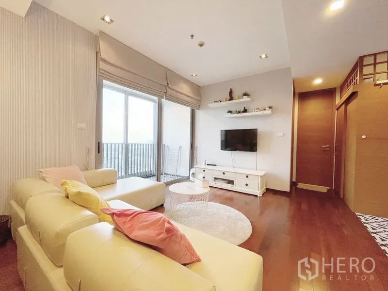 公寓 出售在Khlong Toei, Bangkok - 明亮客厅，奶油色沙发、壁挂电视，推拉玻璃门通往阳台。