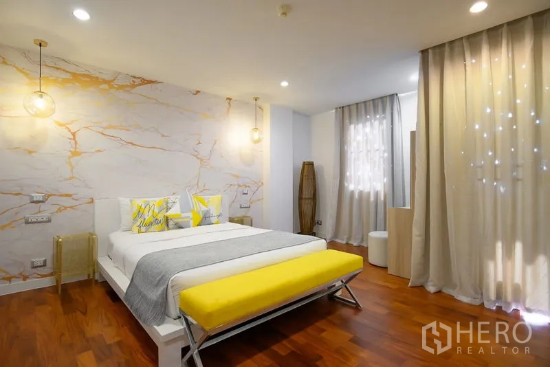 Condominium for rent in Pathum Wan, Bangkok - Contemporary bedroom with marble-effect feature wall, yellow bench, and soft curtains.