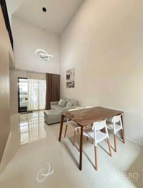 联排别墅 出租在Bang Phli, Samut Prakan - 餐区，木桌、高挑层高与门口的纱帘。