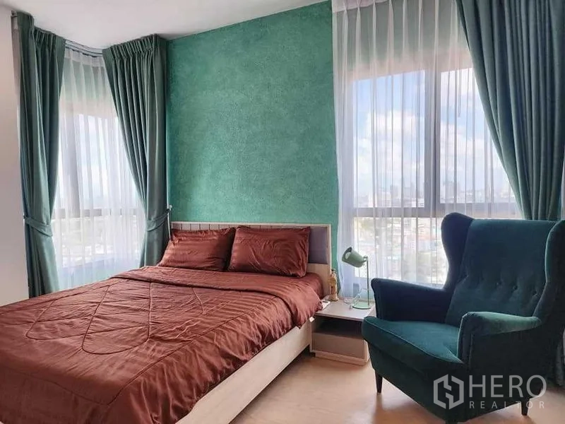 公寓 出租 - 主卧配绿色强调墙、棕色床品与单人沙发，落地窗城市景观。