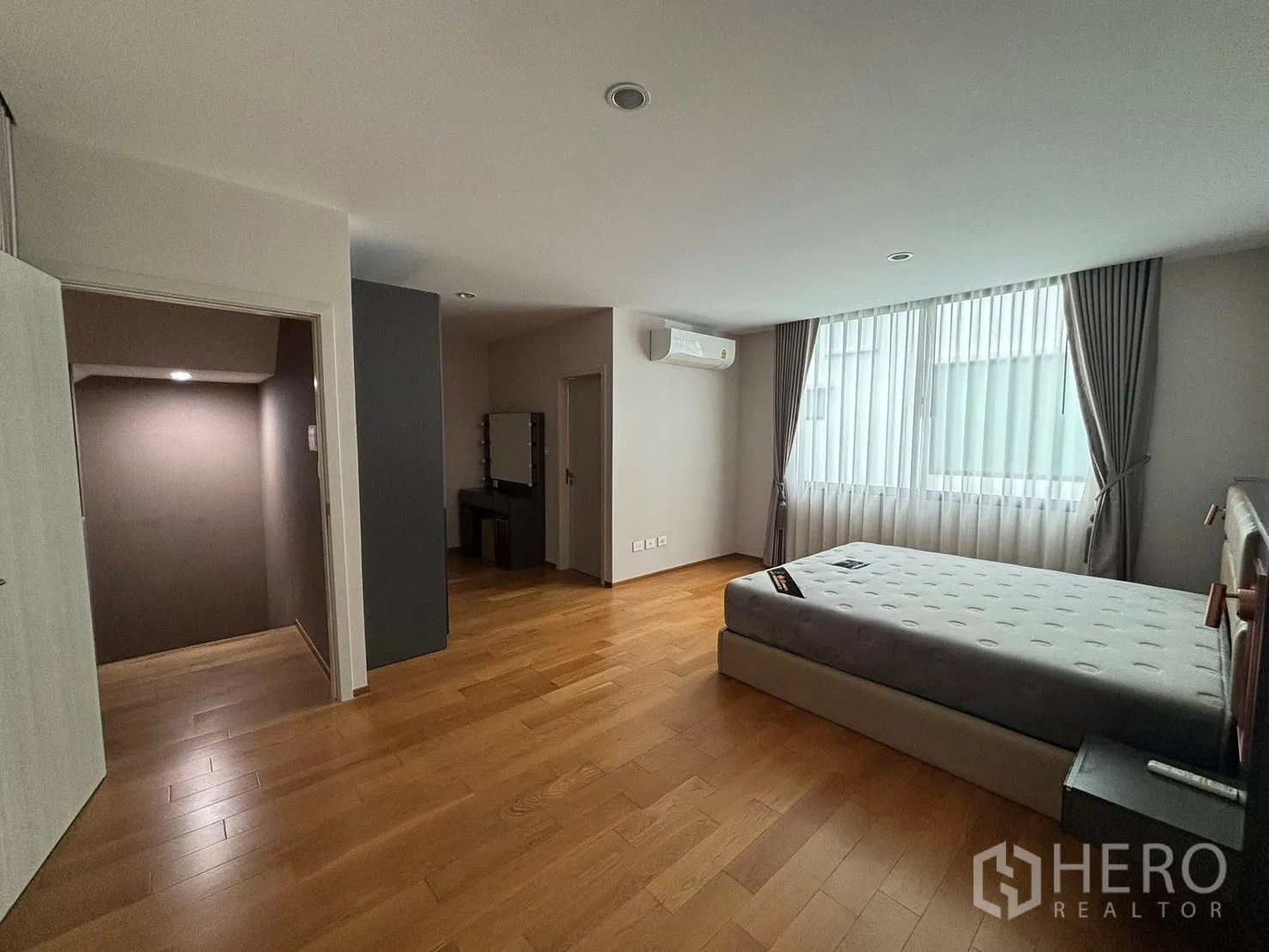 Townhouse for rent in Saphan Sung, Bangkok - Spacious bedroom with wood flooring, bed, large curtained window, and air conditioner.