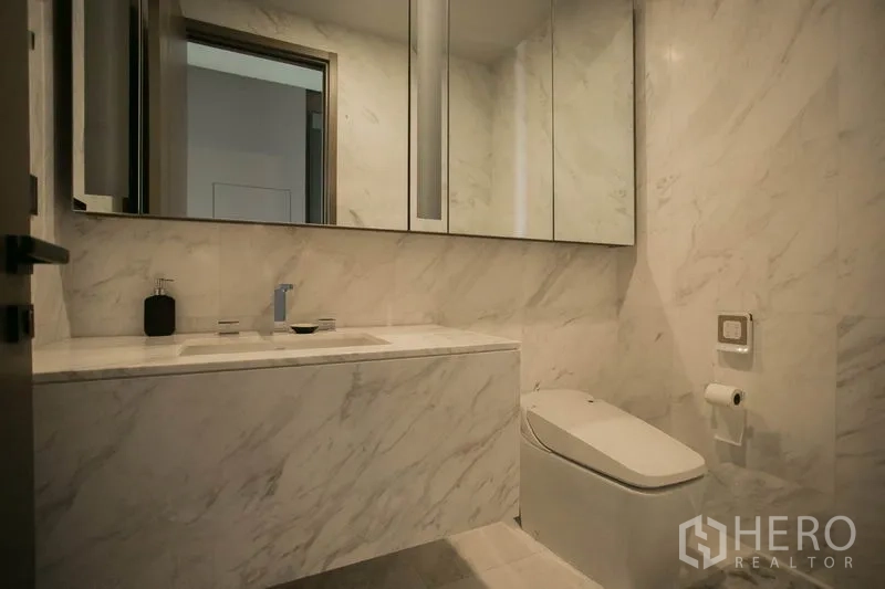 Condominium for rent or sale in Watthana, Bangkok - Guest bathroom finished in white marble with mirrored cabinets and modern toilet.