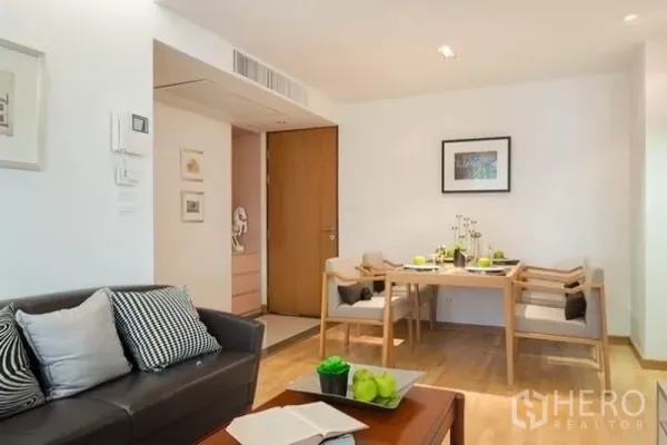 คอนโด ให้เช่าหรือขายในPhra Khanong, Bangkok - ห้องนั่งเล่นอบอุ่น โซฟาหนังพร้อมหมอนอิง และชุดโต๊ะอาหารไม้ 4 ที่นั่งใต้ไฟดาวน์ไลท์.