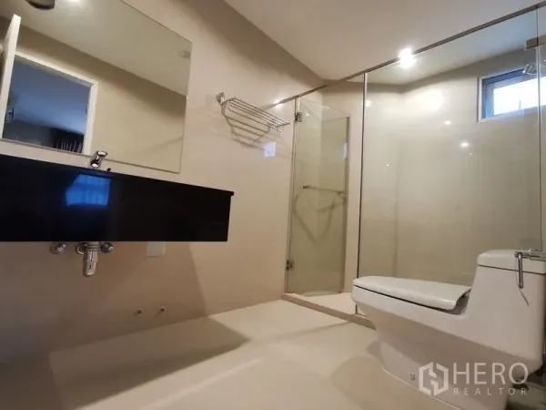 Condominium for rent or sale in Huai Khwang, Bangkok - Bright bathroom with glass shower, wall-mounted black vanity, and toilet in a modern Huai Khwang condo.