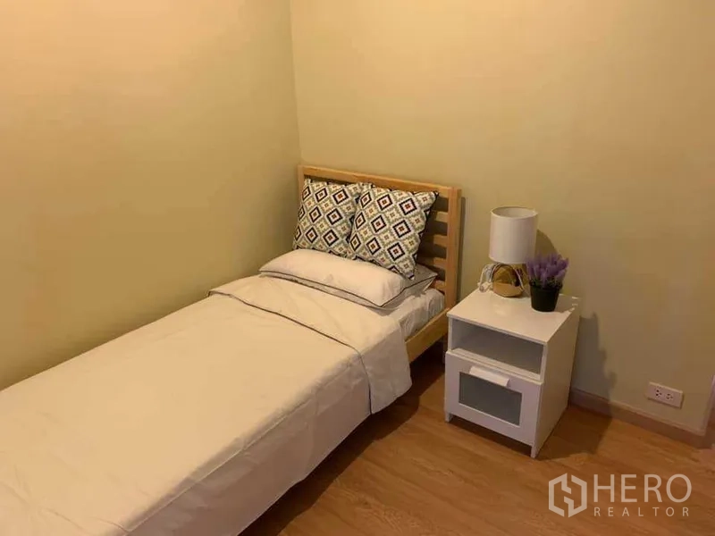 คอนโด ให้เช่าในWatthana, Bangkok - ห้องนอนรอง เตียงเดี่ยว ชุดผ้าปูสีขาว โต๊ะข้างเตียงและโคมไฟ พื้นไม้