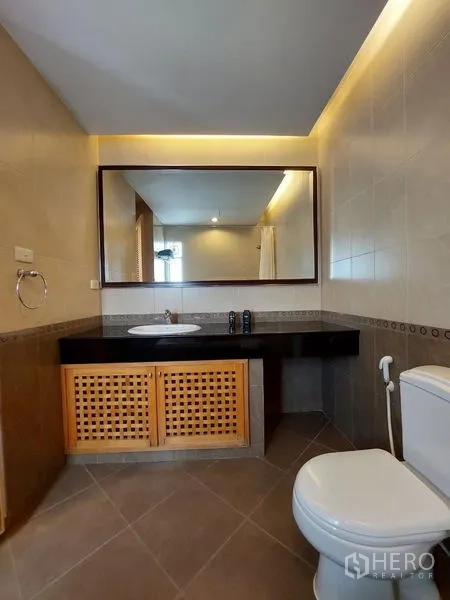 อพาร์ทเมนท์ ให้เช่า - ห้องน้ำที่สอง มีกระจกบานใหญ่ ไฟส่องสว่าง เคาน์เตอร์อ่าง และโถสุขภัณฑ์.