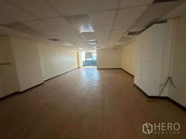 Office Space for rent - Open-plan office with wood-look flooring, drop ceiling lighting, built-in cabinet and windows at the far end.