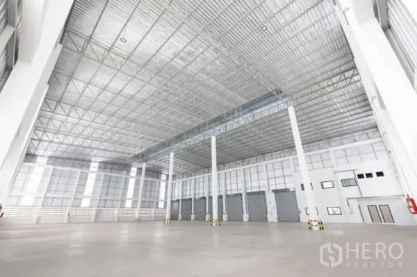 Warehouse for rent in Bang Bo, Samut Prakan - Spacious warehouse interior featuring high steel truss ceiling, multiple dock doors and white columns.