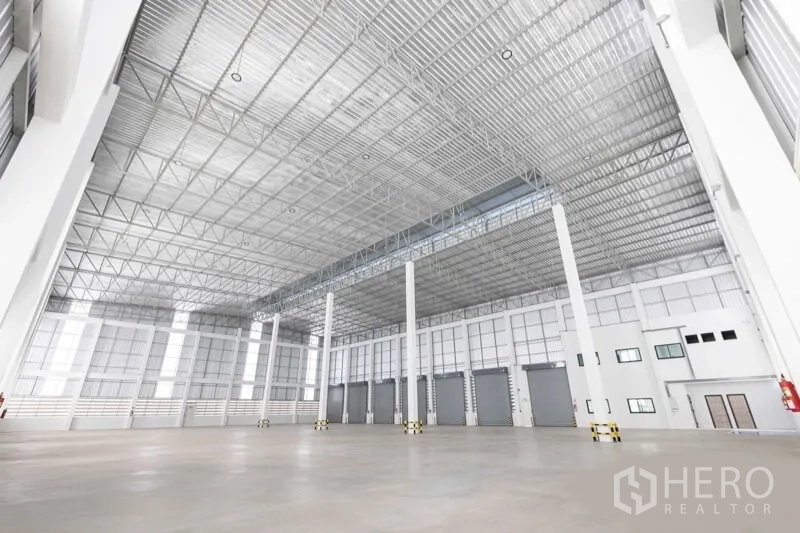 Warehouse for rent in Bang Bo, Samut Prakan - Spacious warehouse interior featuring high steel truss ceiling, multiple dock doors and white columns.