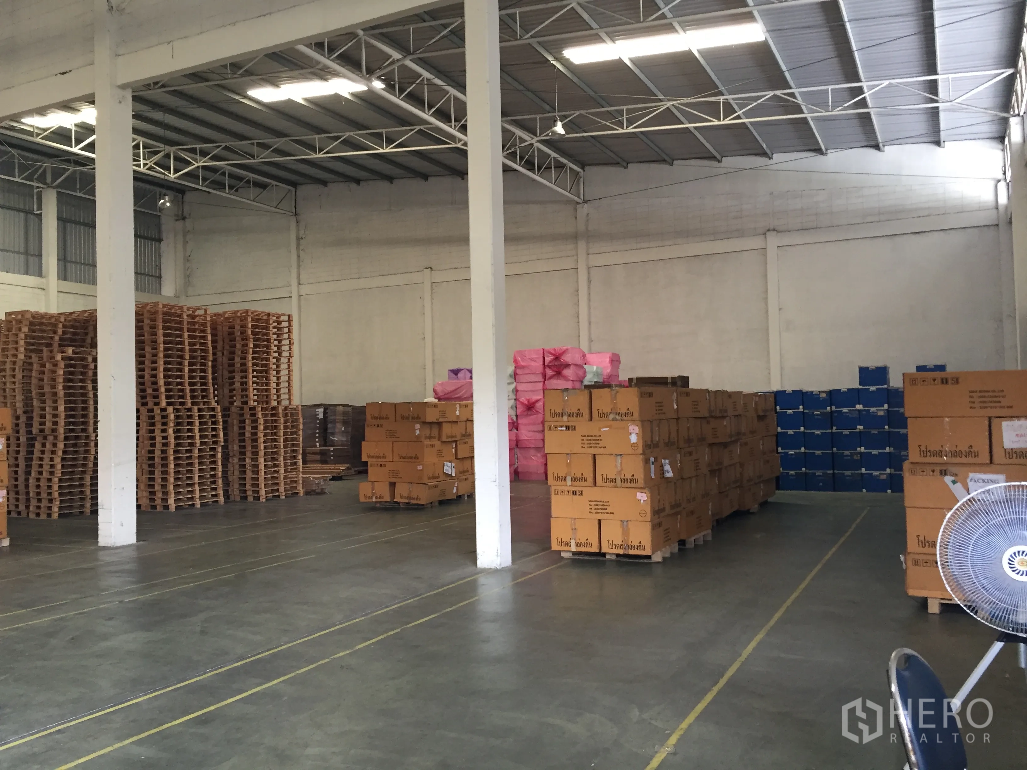Warehouse for rent in Chon Buri - Spacious warehouse interior with high steel-truss ceiling, skylights, polished concrete floor, and palletized boxes.