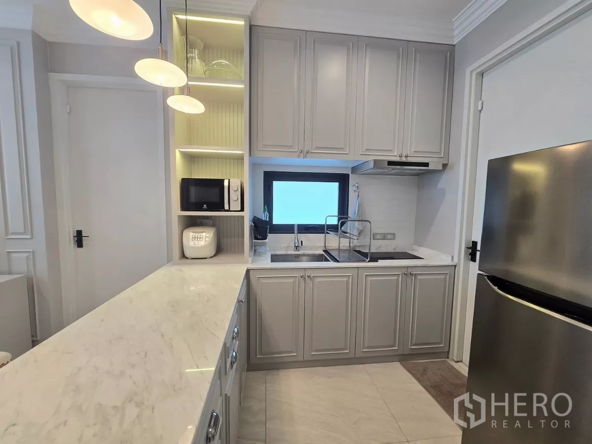 Detached House for rent in Prawet, Bangkok - Compact U‑shaped kitchen with marble countertop, gray cabinets, microwave and stainless fridge.
