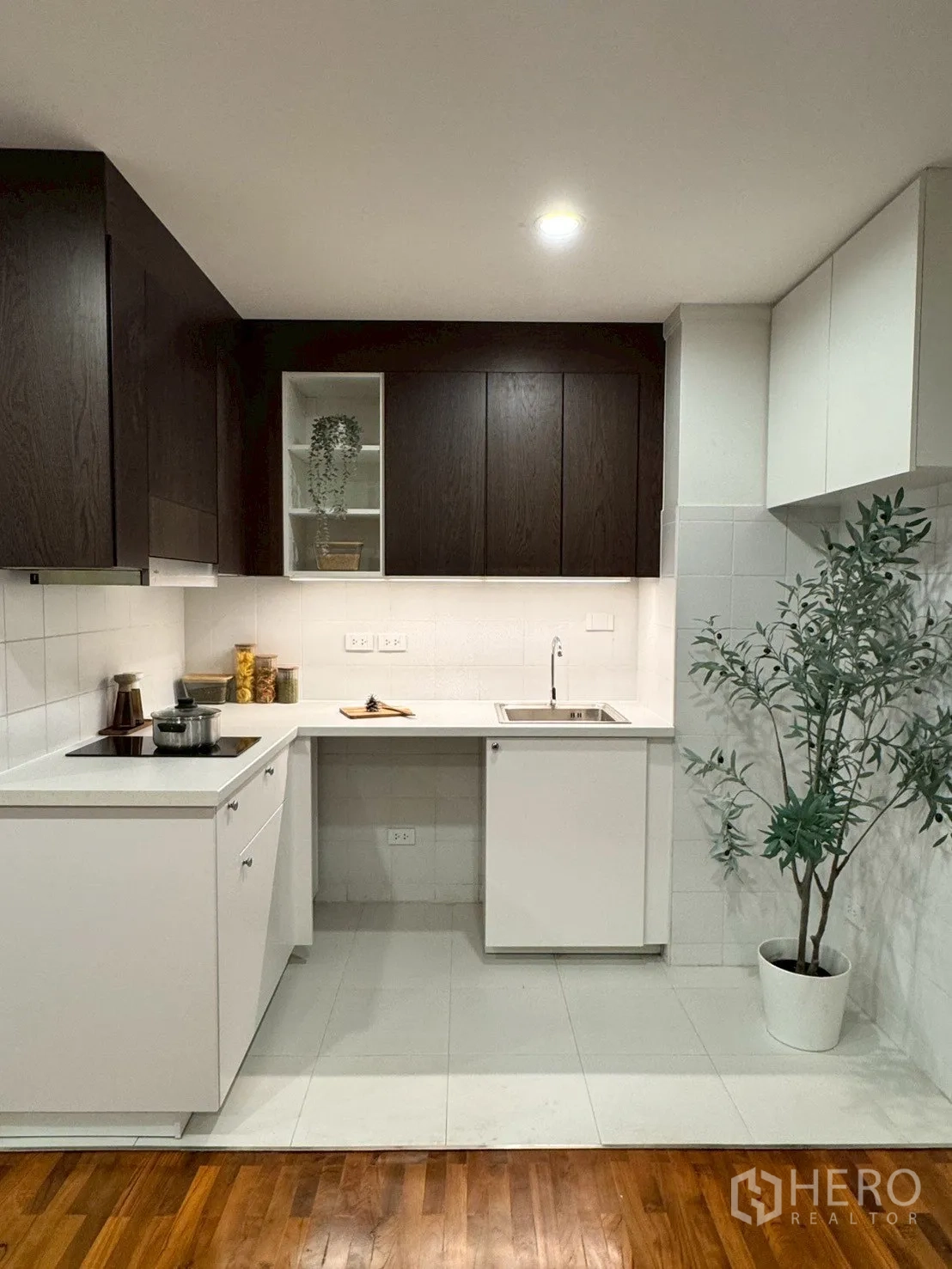 Condominium for sale in Watthana, Bangkok - Compact L-shaped kitchen with dark wood cabinets, white countertops, induction cooktop, and sink.