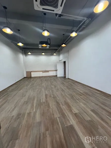 零售空间 出租 - 开阔平面空间，挑高天花吊灯，木纹地面，后方设储物工作台。