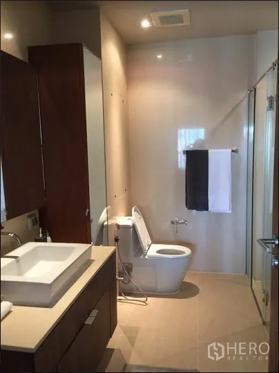 Condominium for rent in Watthana, Bangkok - Contemporary bathroom with vanity, toilet and a glass-enclosed shower.
