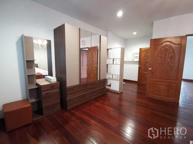 Detached House for rent in Prawet, Bangkok - Upstairs dressing space with polished wooden floors, mirrored wardrobe and carved wooden doors.