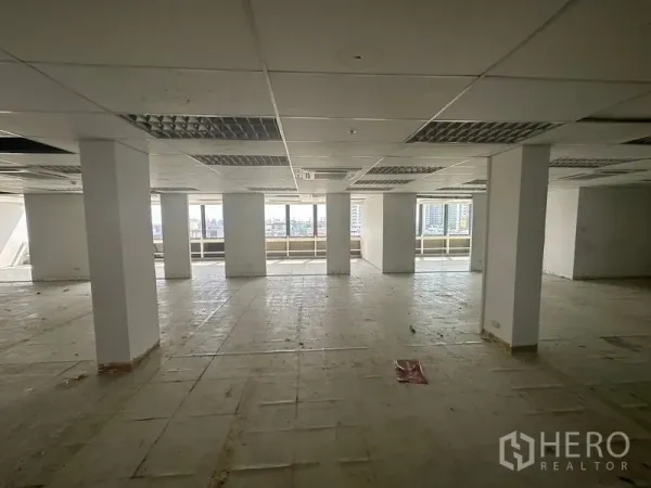 Office Space for rent in Khlong Toei, Bangkok - Open-plan office floor with columns, suspended ceiling and wide windows overlooking the Bangkok skyline.
