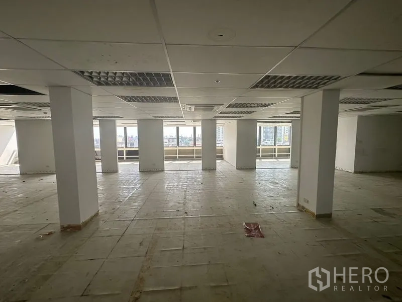 Office Space for rent in Khlong Toei, Bangkok - Open-plan office floor with columns, suspended ceiling and wide windows overlooking the Bangkok skyline.