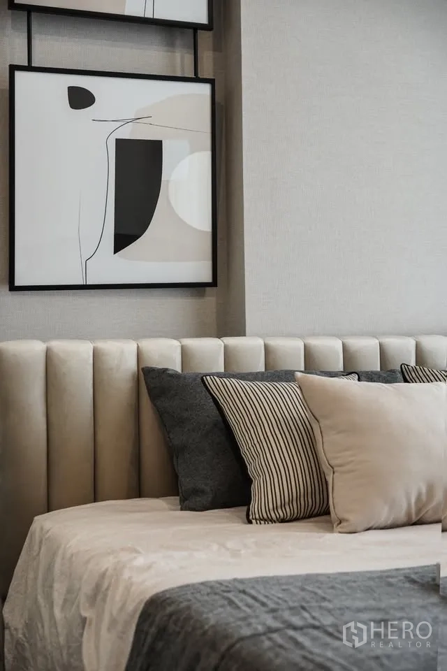 Condominium for rent in Watthana, Bangkok - Stylish bedroom detail showing upholstered headboard, layered pillows, and abstract wall art.